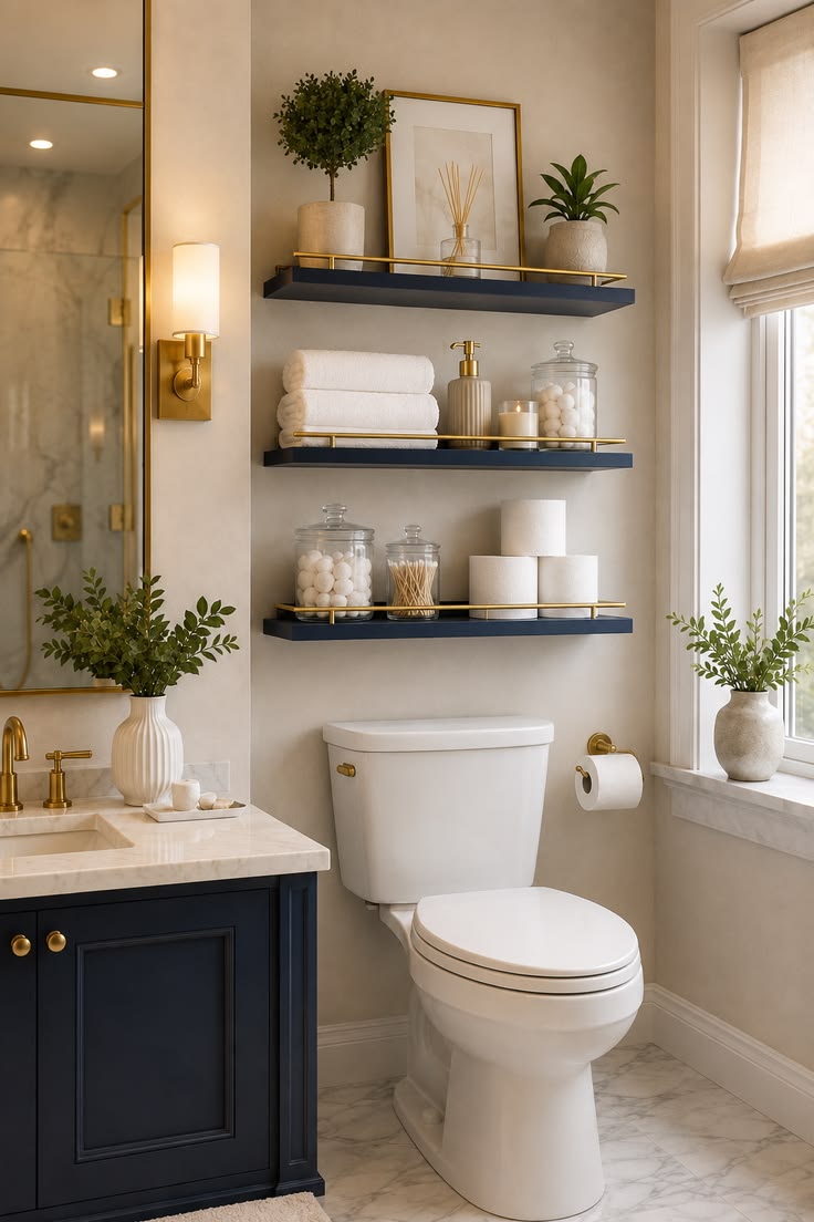 Navy blue floating shelves with gold trim above a toilet in a powder room, styled with plants, frames, jars and toilet paper rolls