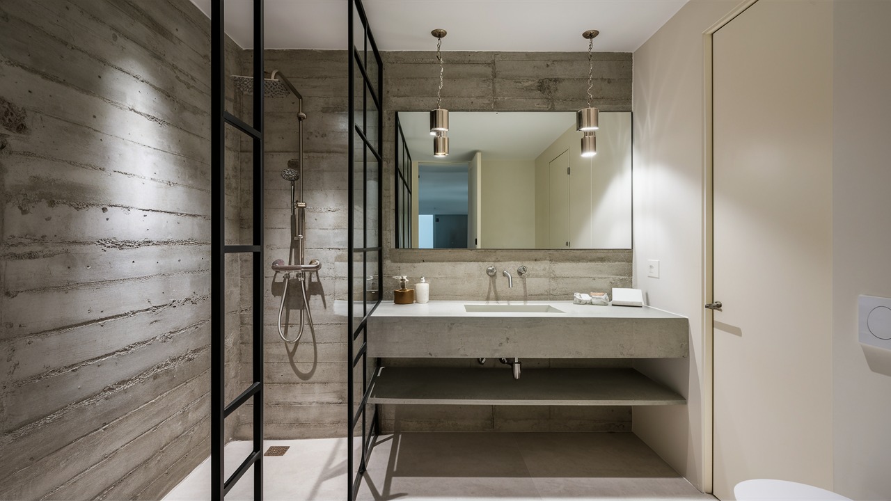 Modern minimalist bathroom with a textured concrete-look accent wall, glass shower enclosure and pendant lights over a floating vanity