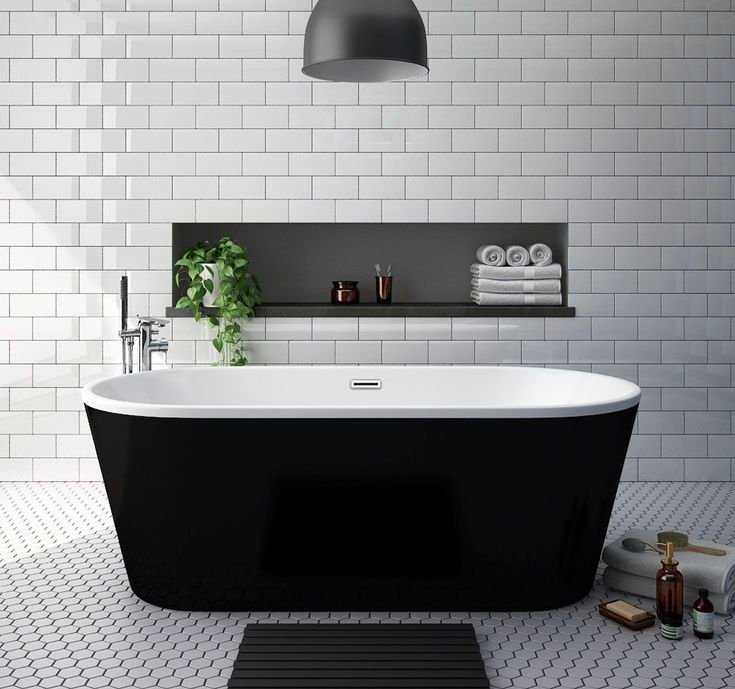 Matte black freestanding tub against white subway tile with a dark built-in niche shelf and black pendant light