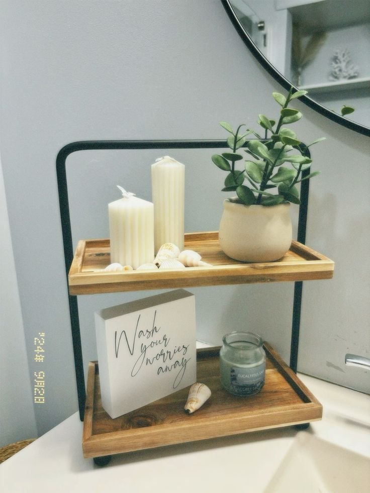 Two-tier wood tray on a bathroom shelf with pillar candles, seashells, a small plant and a wash your worries away sign