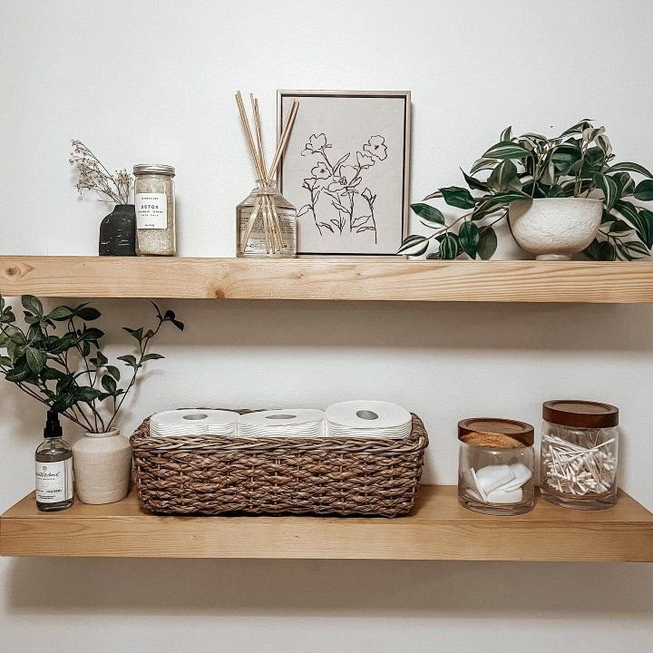 Light wood tiered bathroom shelves styled with a wash brush floss flush sign, trailing succulents, a wood knot object and a small potted plant