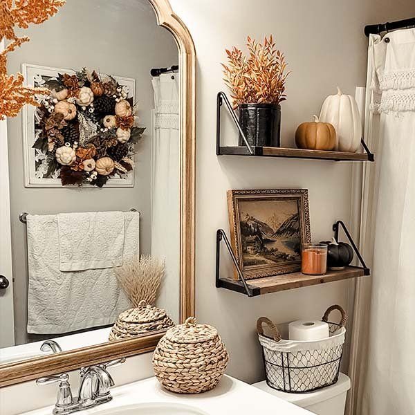 Bathroom shelves styled with a fall wreath, a small pumpkin, dried branches and a framed landscape print
