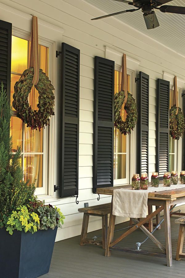Matching wreaths hung on dark shutters along a row of windows above an outdoor dining table