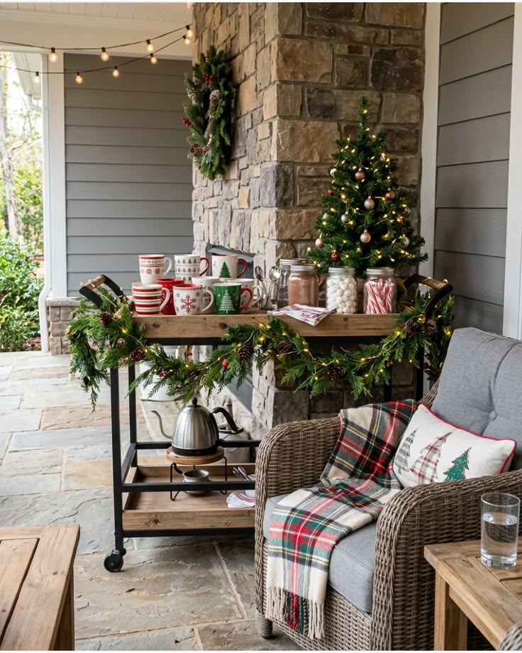 A bar cart styled as a hot cocoa station with mugs, marshmallows, candy canes and a kettle beside a wicker chair with a plaid throw