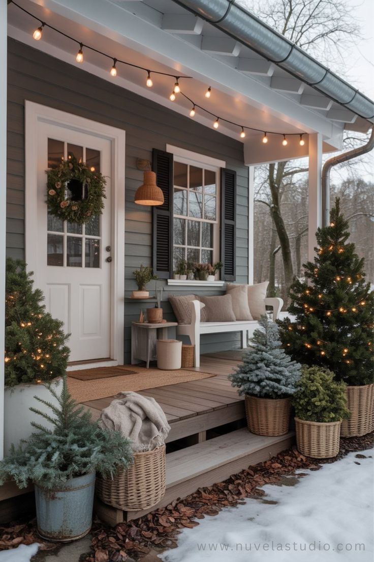 Three small Christmas trees of different heights in woven baskets beside a bench with pillows and string lights