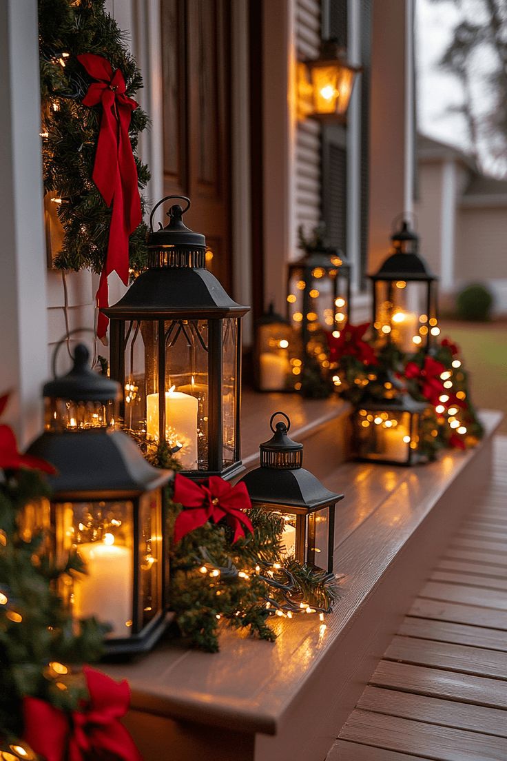 A row of black lanterns with candles, red bows and greenery lined up along a porch railing