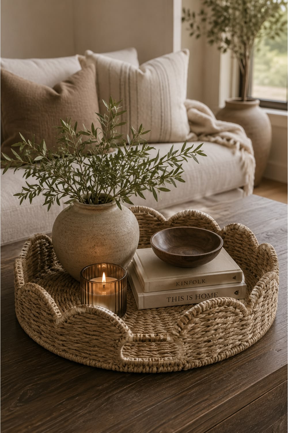 Woven tray with a vase, candle, books and a small wooden bowl on a coffee table