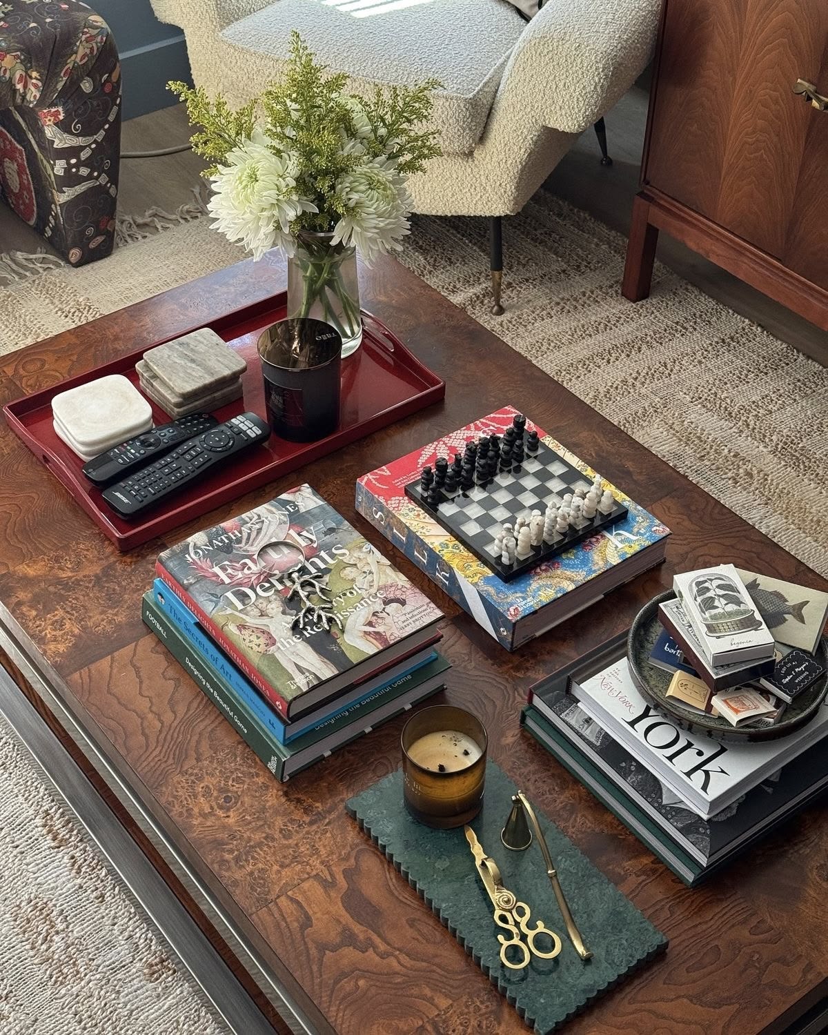 Coffee table with remote controls and coasters organized on a red tray beside book stacks