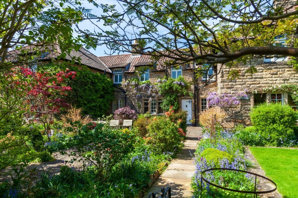 English stone cottage with wisteria climbing the facade, surrounded by a layered informal garden with a stone path leading to the front door