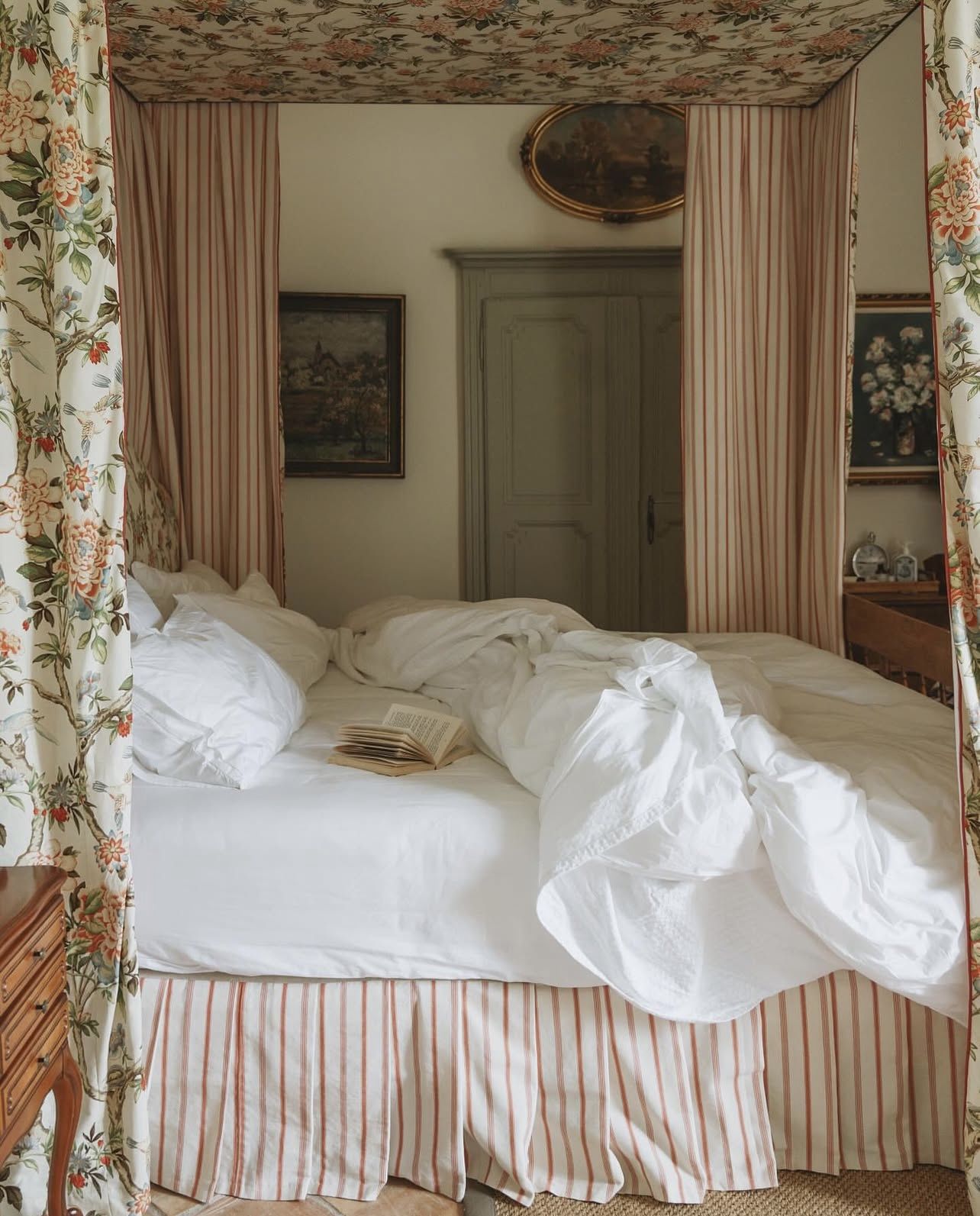 Four-poster bed draped in floral fabric with striped curtains in a cottagecore bedroom