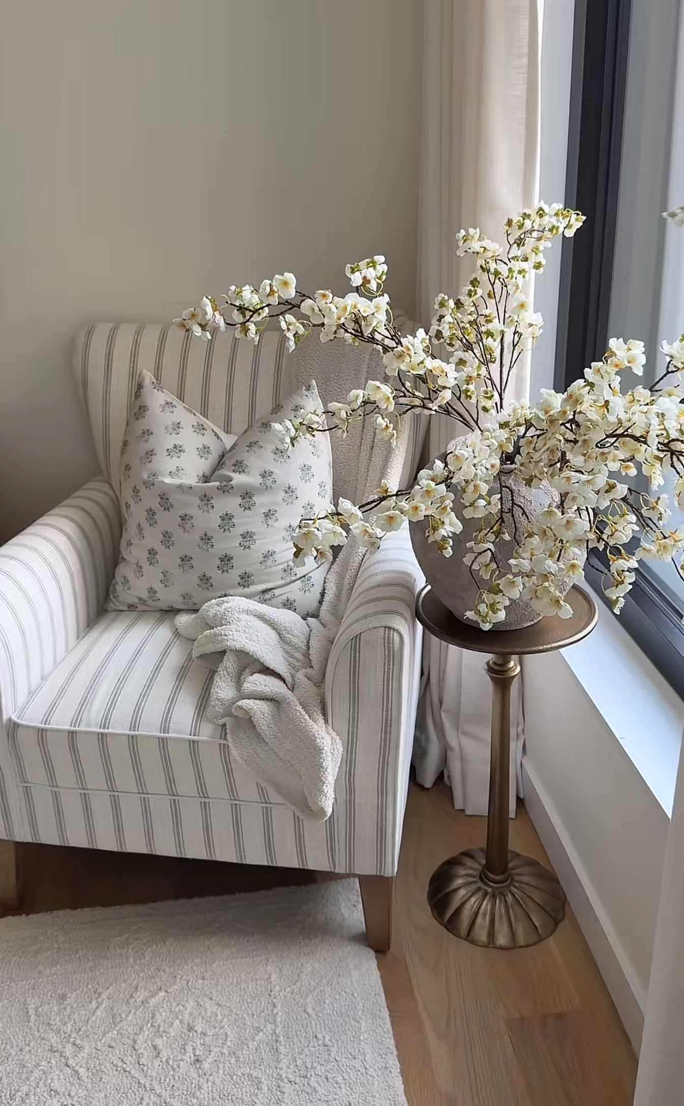 Striped armchair with a block-print pillow and a vase of blossoming branches beside a window