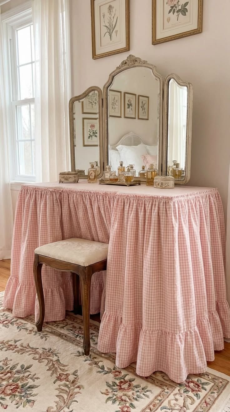 Pink gingham skirted vanity table with a ruffled hem, antique tri-fold mirror, botanical prints and perfume bottles
