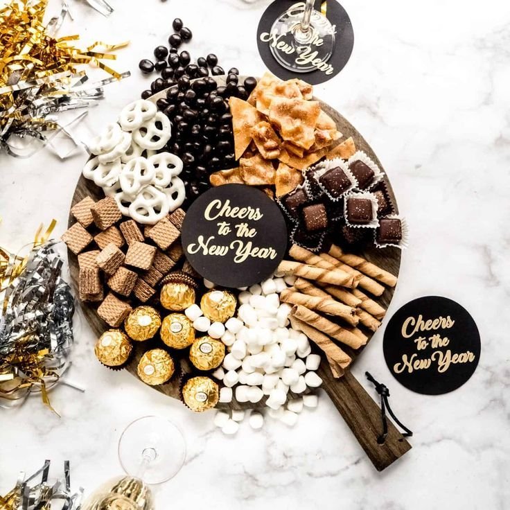 Elegant black and gold New Year's dessert board with Ferrero Rocher, chocolate-covered pretzels, wafer bars and chocolate truffles on a dark wood board