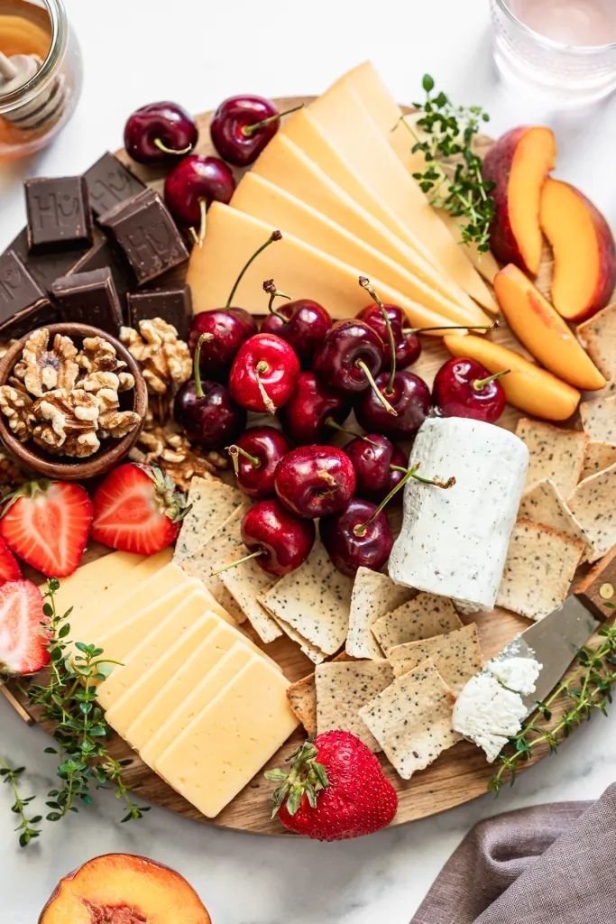 Summer fruit board with fresh cherries, sliced peaches, strawberries, cheese slices, crackers and walnuts on a round wood board