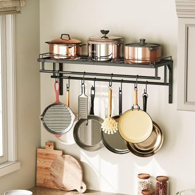 Wall-mounted metal rack with a row of hooks holding hanging pots, pans and utensils above a kitchen counter with cutting boards
