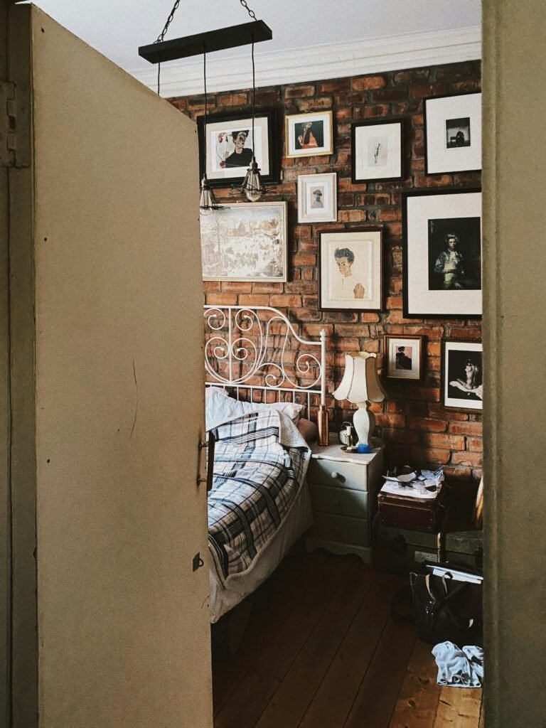 Framed black-and-white art prints and photos arranged in a gallery wall on an exposed brick wall above a white iron bed frame