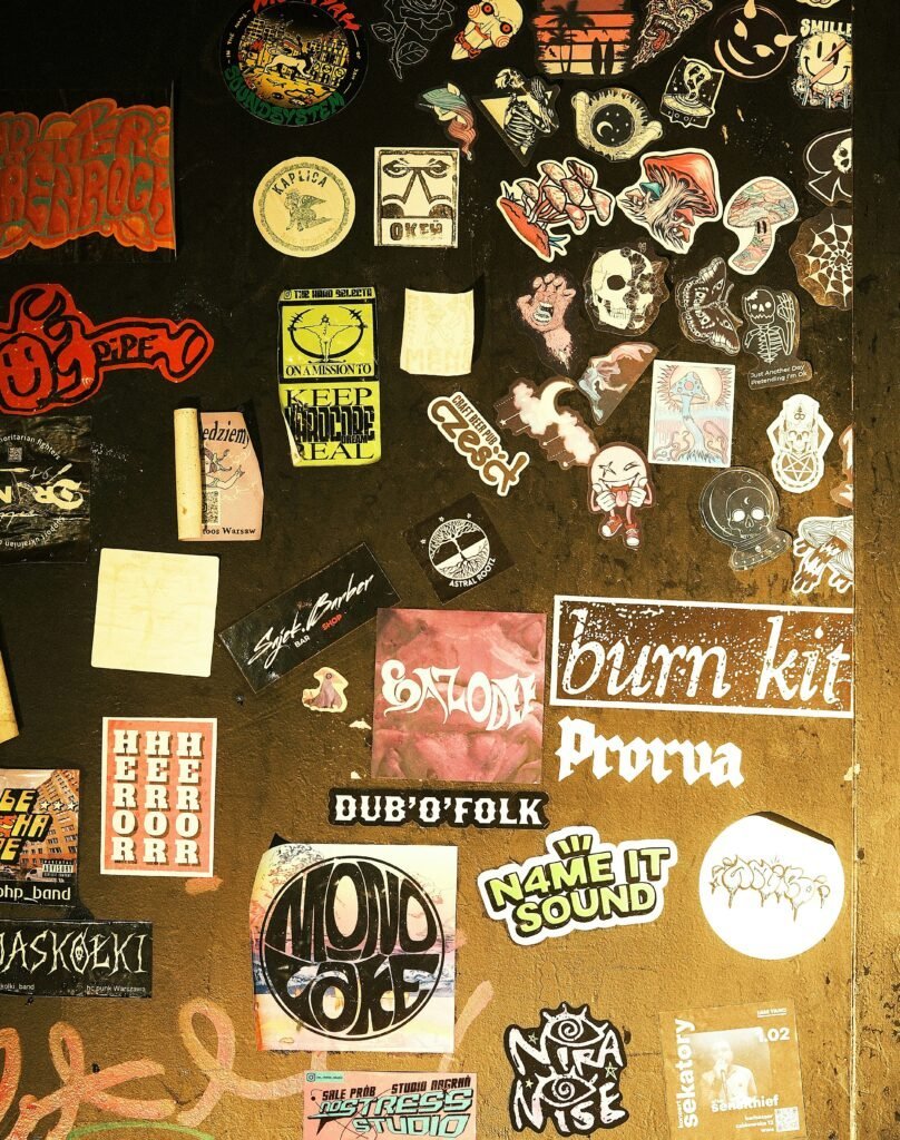 Wall densely covered edge to edge with band stickers, patches and punk show flyers in a dorm room