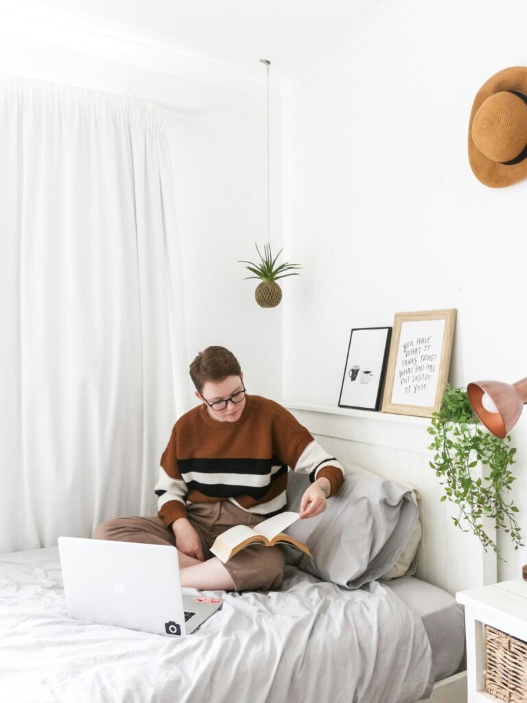 Minimalist bedroom corner with two small framed prints, a hanging air plant and a straw hat styled above a narrow shelf beside a bed
