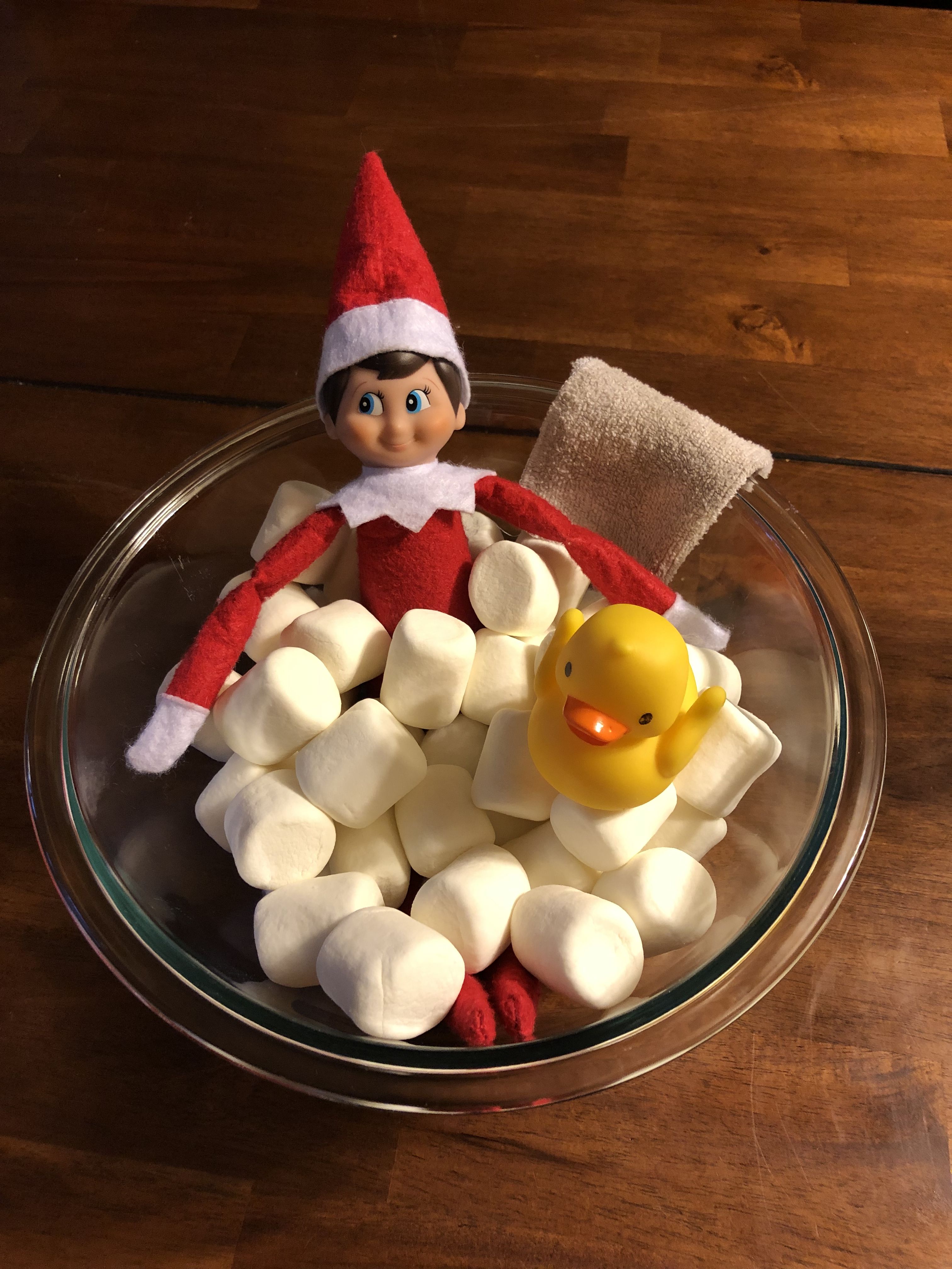Elf on the Shelf sitting in a glass bowl filled with mini marshmallows and a rubber duck to look like a bubble bath