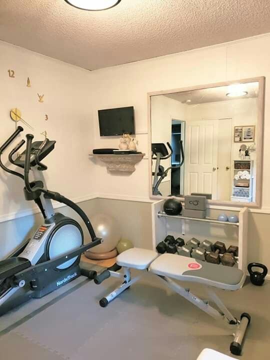 Small home gym corner fitted with an elliptical, weight bench, dumbbell rack and wall mirror