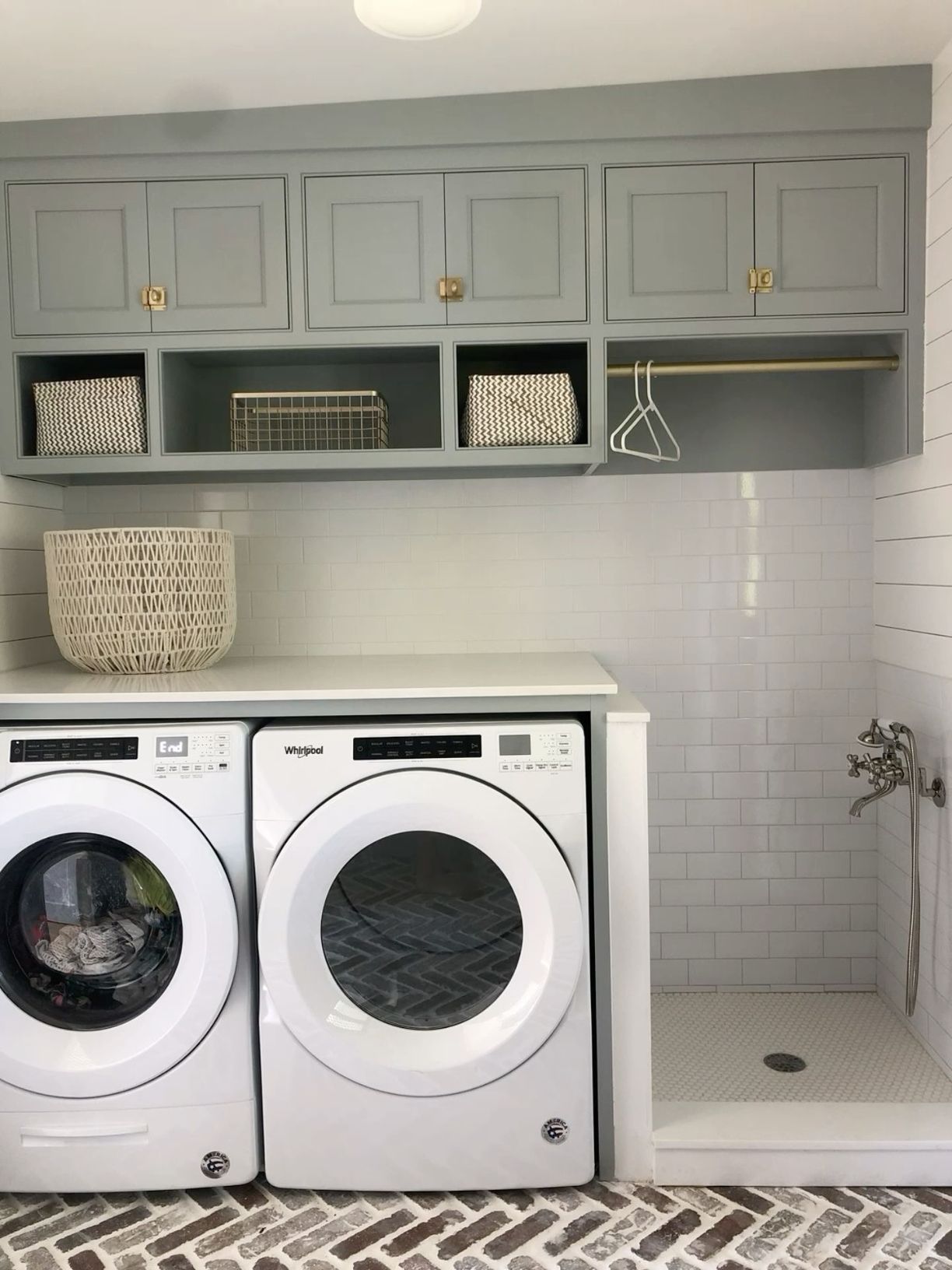 Tiled walk-in pet washing station with a handheld sprayer beside a laundry room's washer and dryer