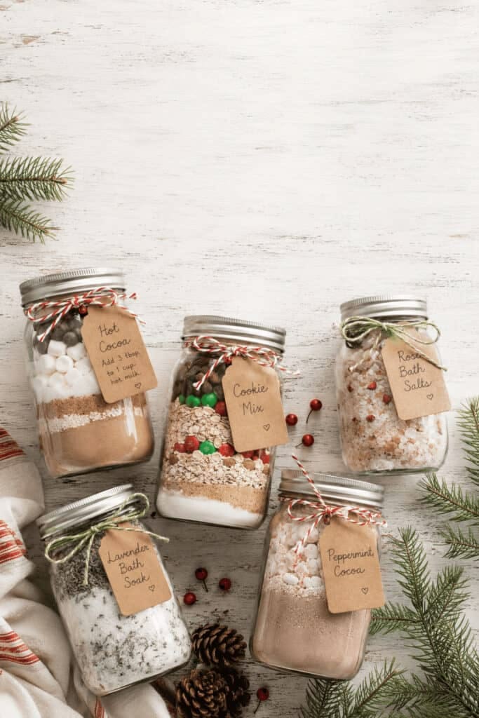 Five labeled Mason jars filled with hot cocoa, cookie mix and bath salts as gifts
