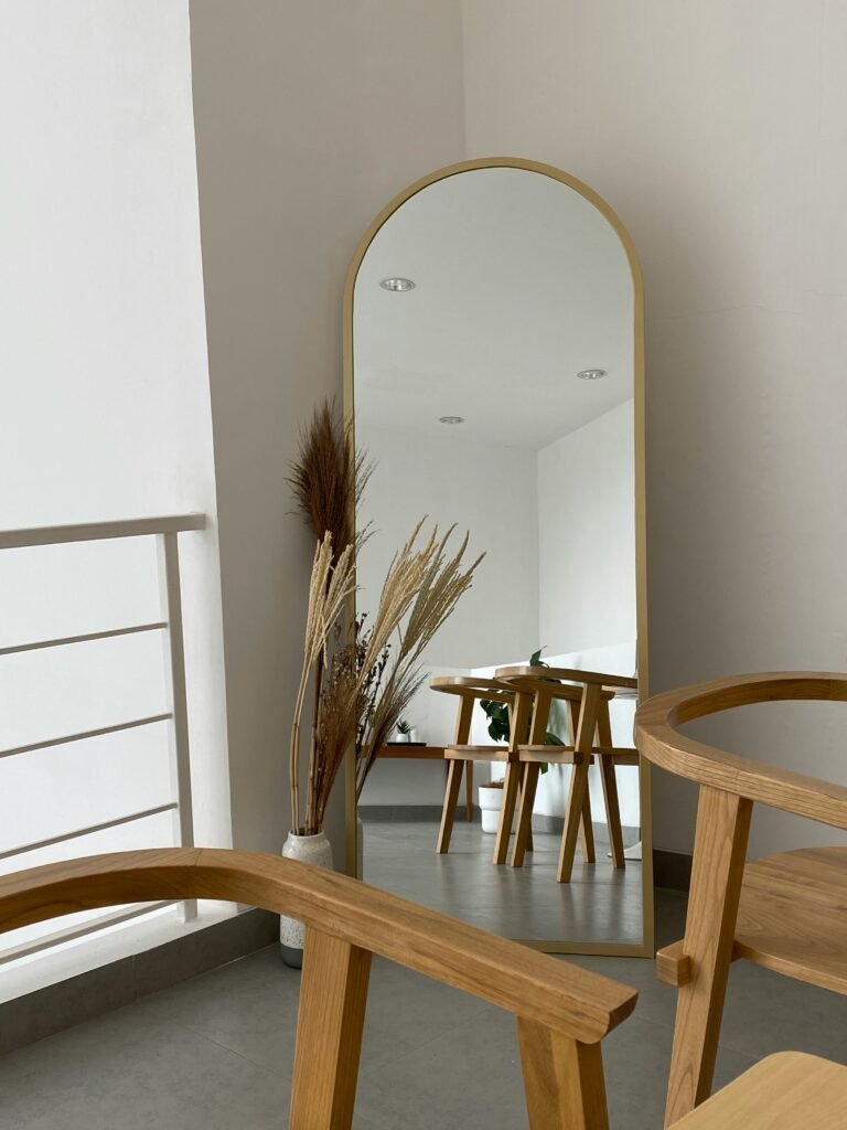 Tall arched mirror with a warm wood-toned frame leaning in a room with wooden furniture