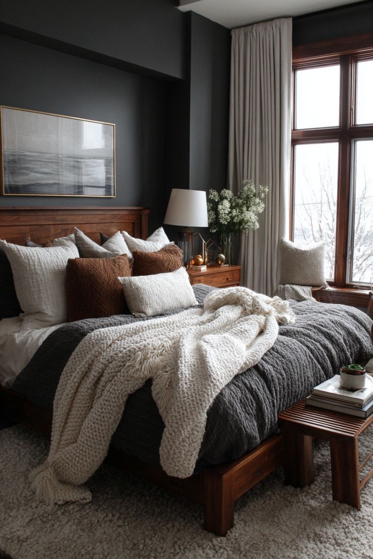 Charcoal gray bedroom walls with a walnut bed frame, gray knit duvet, cream and rust pillows and a chunky throw