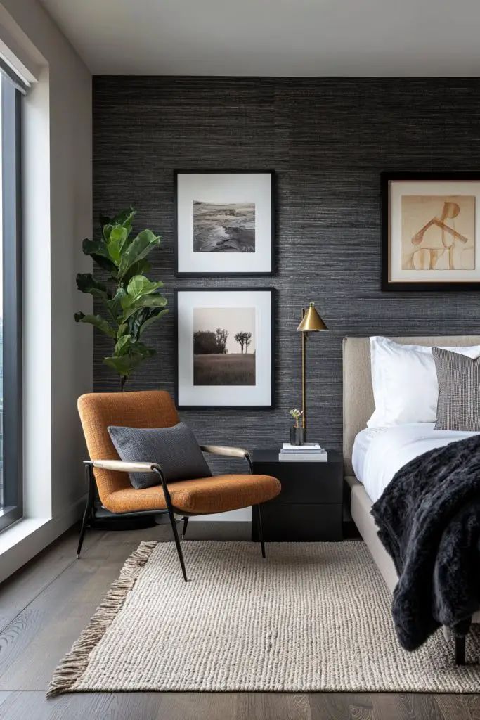 Charcoal grasscloth textured wallpaper behind a bed, with framed landscape photography, a rust chair and a brass lamp
