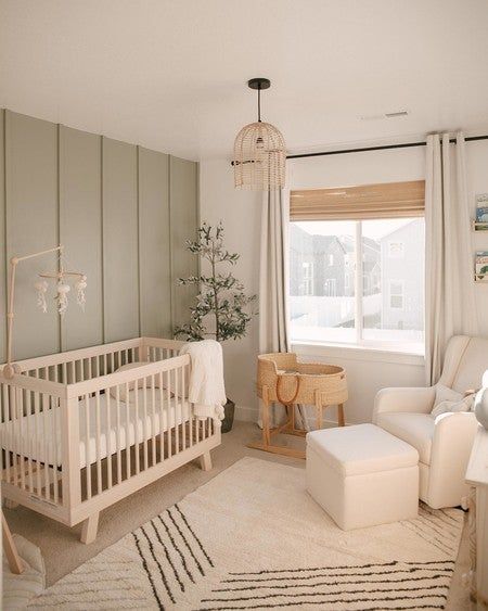 Cozy sage green nursery with a white crib, woven baskets and a soft rug