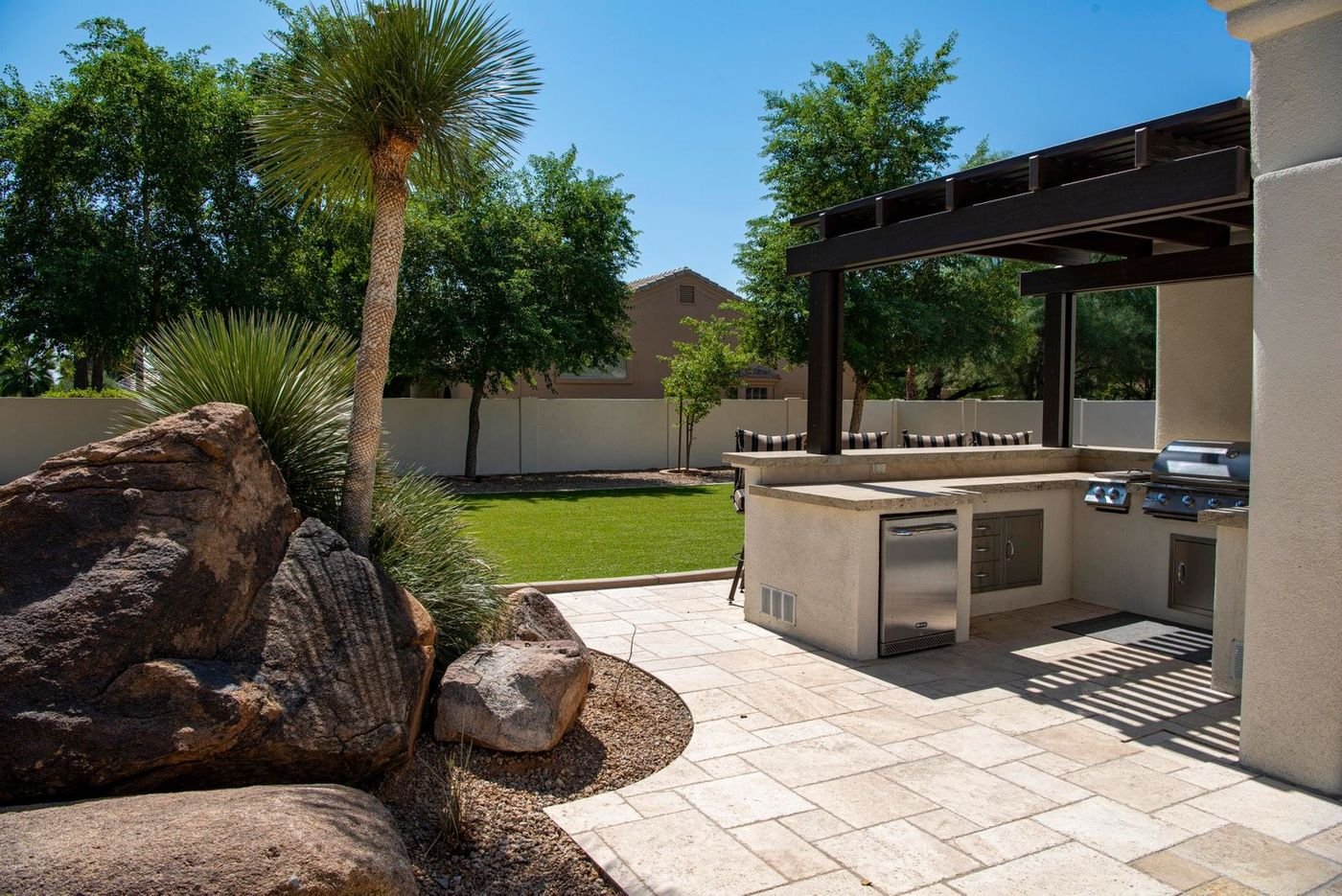 Built-in outdoor kitchen with a pergola, grill and stone countertop in a desert backyard