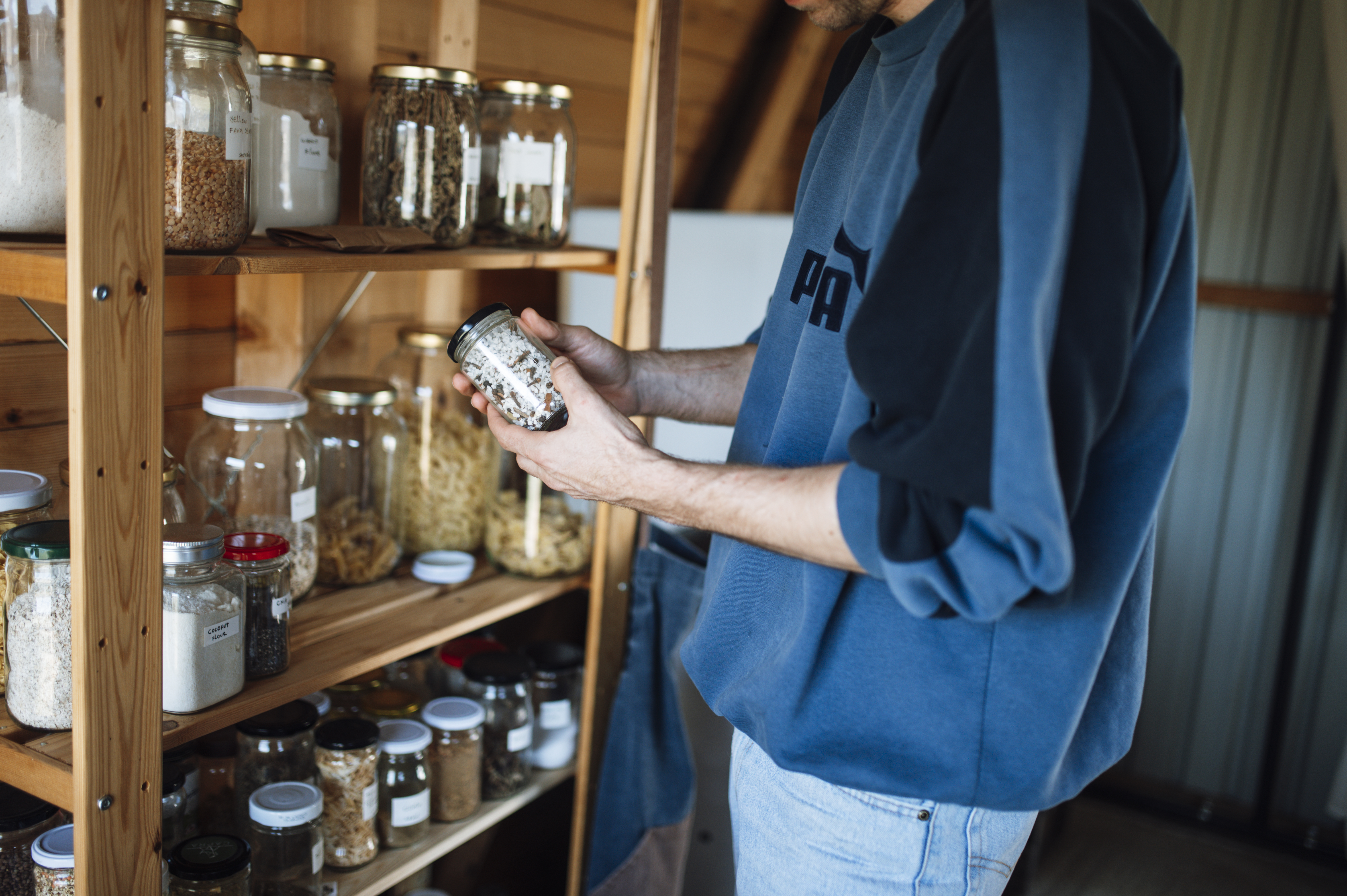 Person examining the label on a spice jar while checking pantry shelves