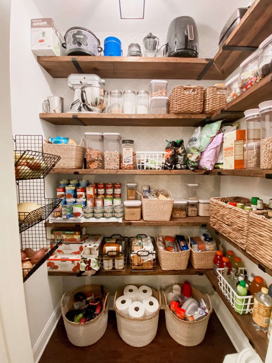 Deep pantry shelving with small appliances, wicker baskets, clear containers and canned goods on a wire riser