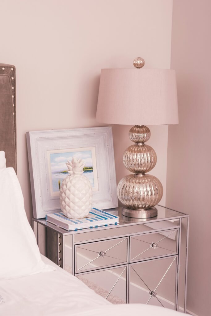 Rose gold mercury glass table lamp and a framed print on a mirrored nightstand against a blush pink wall