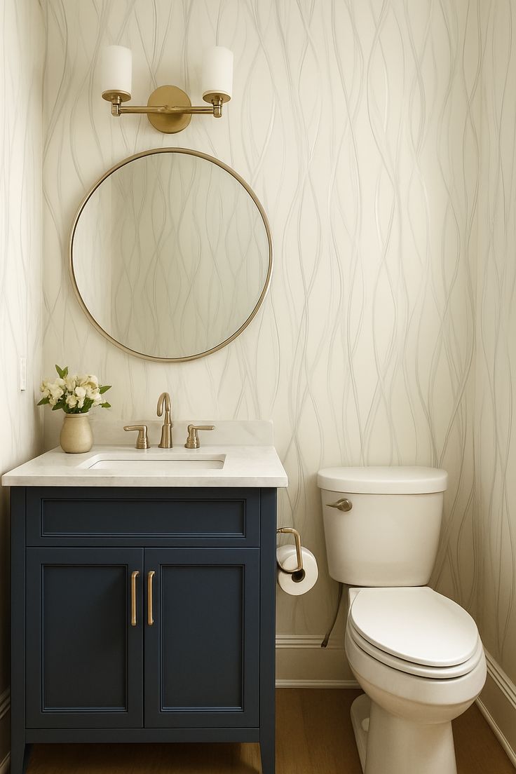 Navy blue vanity with a round brass mirror, brass faucet and brass toilet paper holder against subtle wave-pattern wallpaper