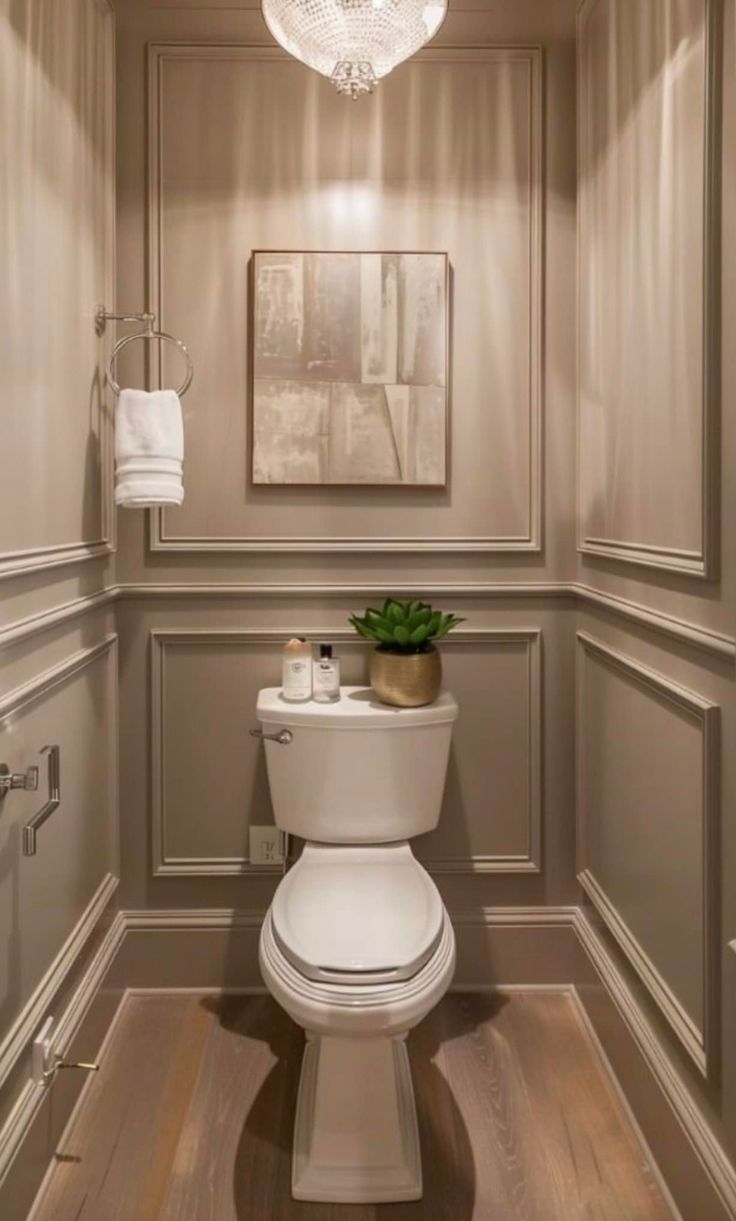 Powder room with box wall molding, a crystal pendant chandelier, framed art and a toilet styled with a small plant
