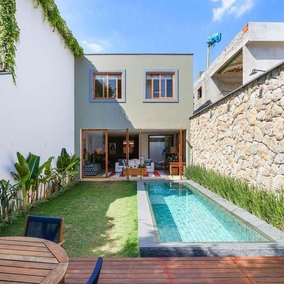 Small narrow backyard pool with a stone wall and wood deck