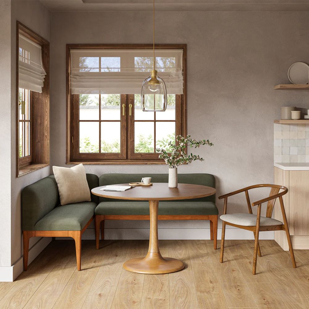 Green built-in banquette tucked into a window corner with a round table and wishbone chair