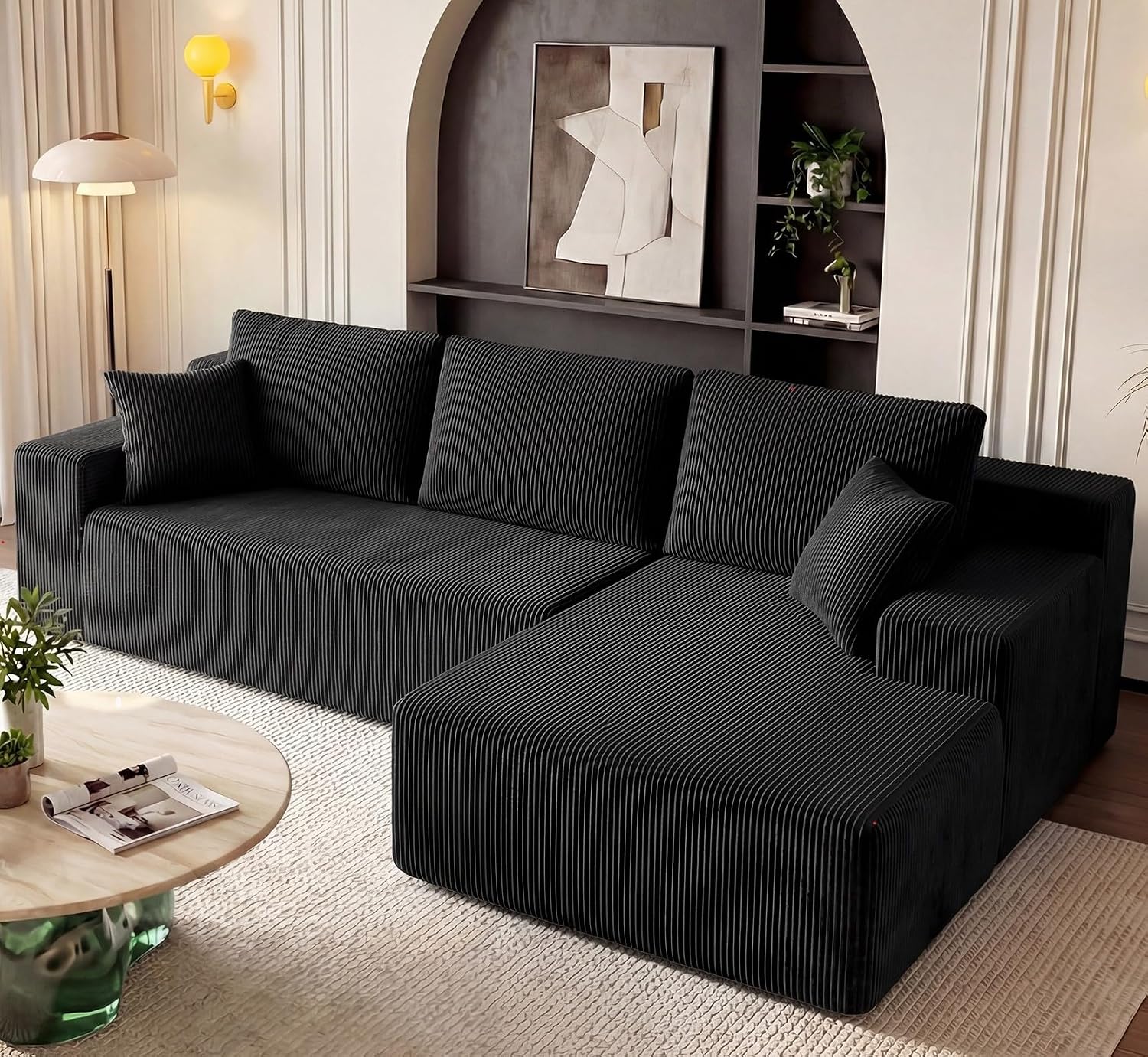 Black corduroy sectional sofa with a deep chaise and a round coffee table in a living room with an arched alcove