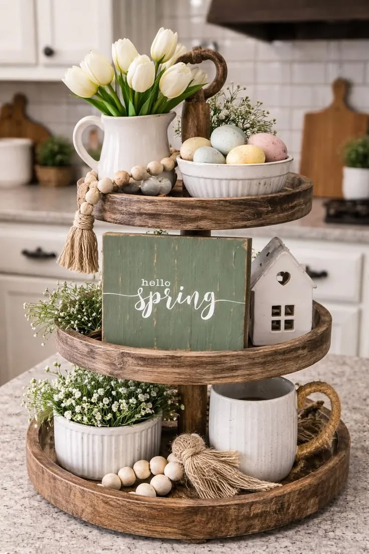 Three-tier wood tray styled with a Hello Spring sign, white tulips, pastel speckled eggs and a small house for spring