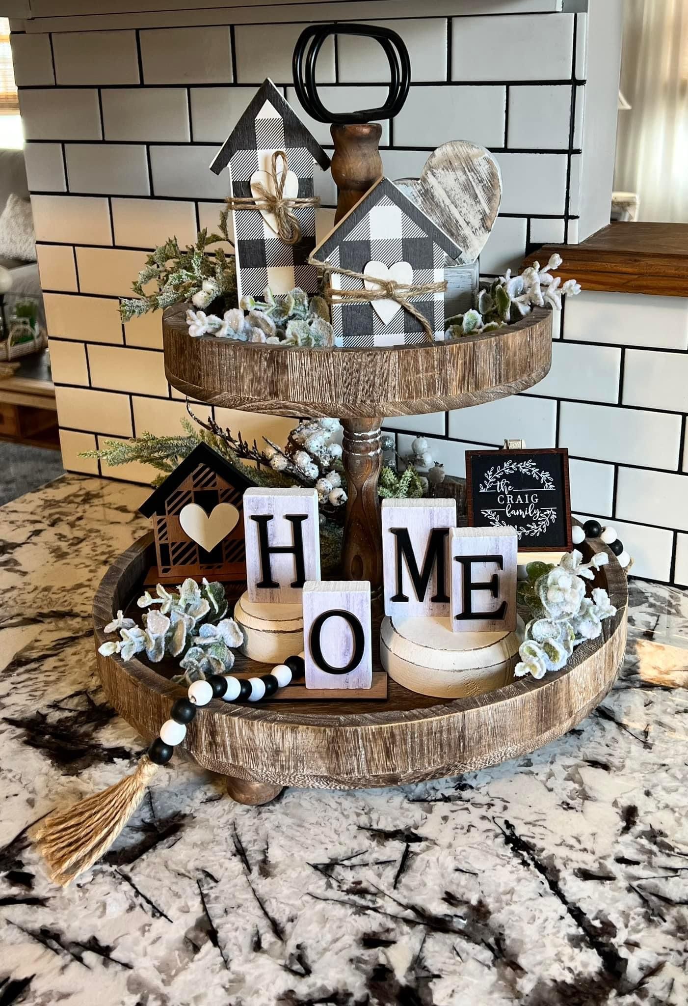 Two-tier black and white buffalo check tray with HOME letter blocks, wood houses and a family name sign against a black and white subway tile backsplash