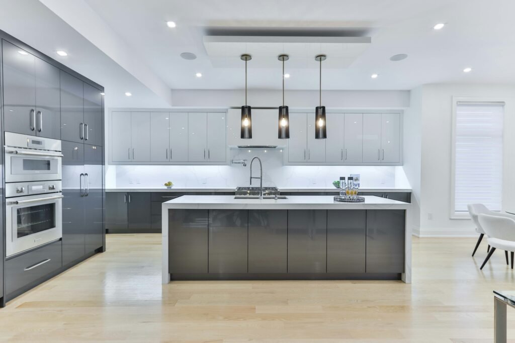 Large modern kitchen with a gray waterfall-edge island, three black pendant lights and glossy gray upper and lower cabinets
