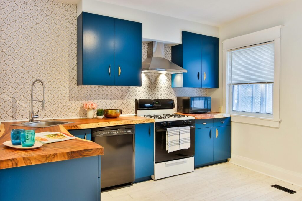 Blue L-shaped kitchen cabinets wrapping around two walls with a wood butcher block corner counter and patterned tile backsplash