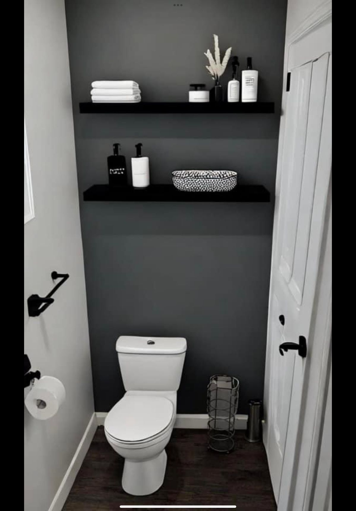 Black floating shelves styled with white towels and a black and white patterned bowl above a toilet