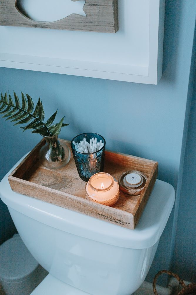 Wooden tray with a lit candle, glass jar and small fern on a toilet tank
