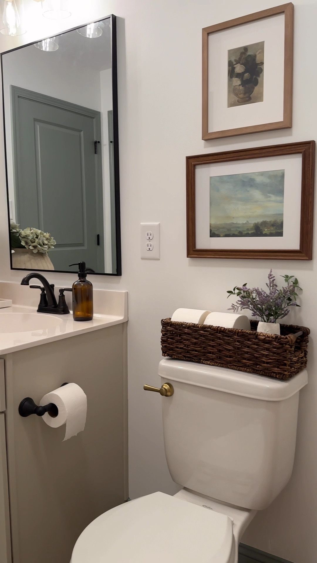 Framed artwork hung above a toilet tank styled with a woven basket and small vase