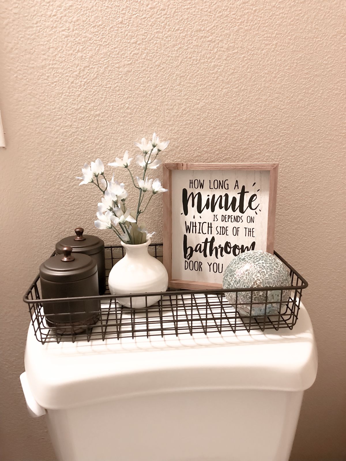 Wire basket with vintage-style canisters, a white vase and a wooden sign on a toilet tank
