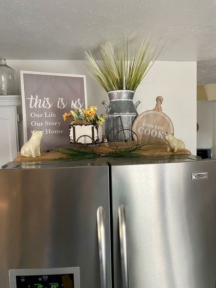Top of fridge styled with a framed sign, greenery and a milk can vase