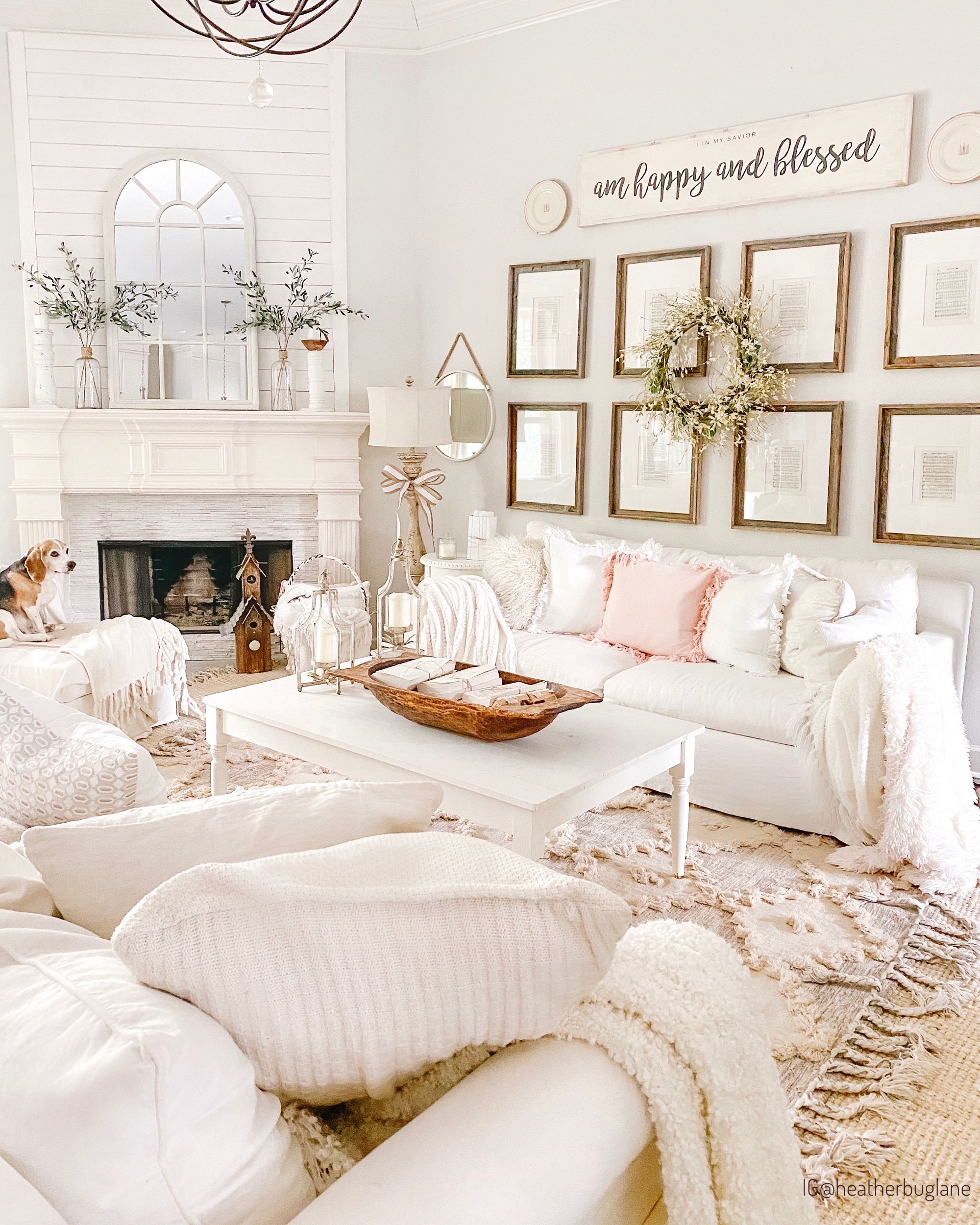White farmhouse living room with a slipcovered sofa, wool rug, gallery of framed sheet music and a wood mantel