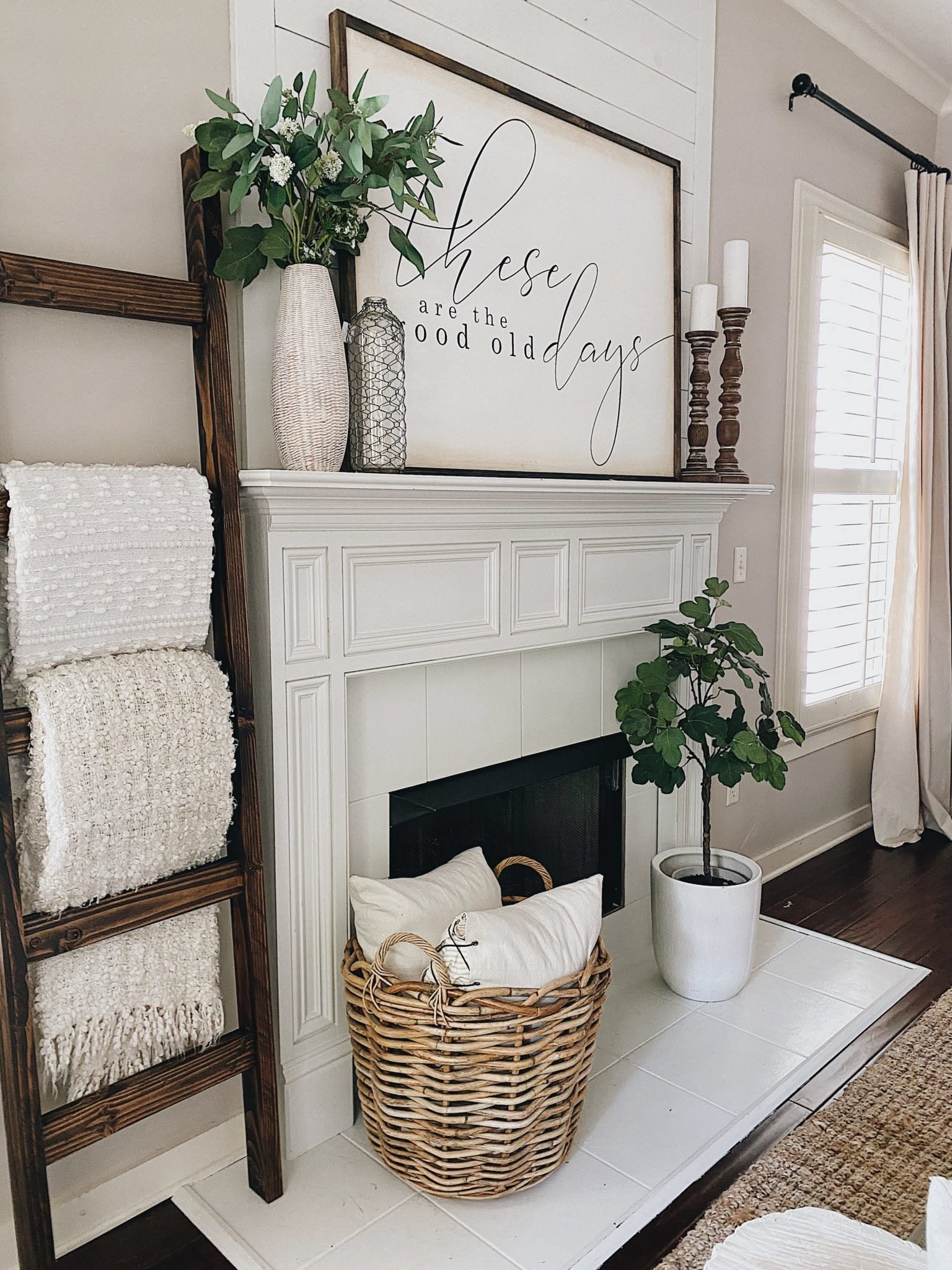 White fireplace mantel styled with a wood ladder holding cream knit throws, a woven basket and a fiddle leaf fig